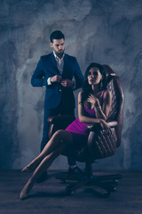 Portrait of sexual hot woman in purple dress sitting in leather chair looking at camera trendy man...