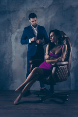 Obraz na płótnie Canvas Portrait of sexual hot woman in purple dress sitting in leather chair trendy man unbutton jacket looking at bitch having erection lovely attractive couple isolated on grey dark background