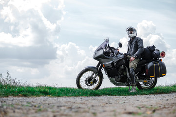 Obraz na płótnie Canvas Rider Man and off road adventure motorcycles with side bags and equipment for long road trip, river and clouds on background, enduro travel touring concept