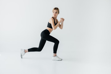 Fototapeta na wymiar Side view of young athletic sportswoman doing lunges isolated on grey