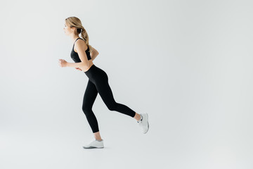 Side view of young athletic sportswoman running isolated on grey