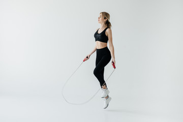 young sportive woman exercising with skipping rope isolated on grey - obrazy, fototapety, plakaty