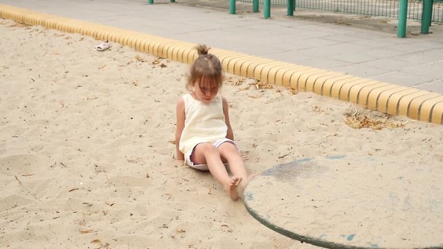 Kid girl funny playing on playground sandbox jumping and falling on a sand