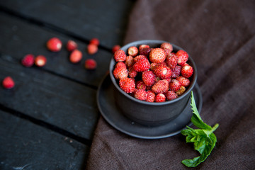 Wild strawberries in a black bowl, dark moody composition with copy space