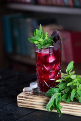 Red cocktail drink in a glass with mint leaves and ice, fresh juice and liquor