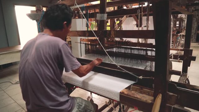 Indonesian man weaving white towel with foot-treadle loom machine. Shot with Sony a7s and Atomos Ninja Flame in Indonesia
