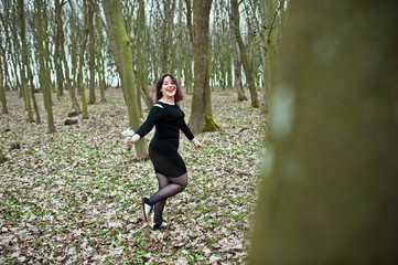 Naklejka na ściany i meble Portrait of brunette girl in black dress at spring wood.