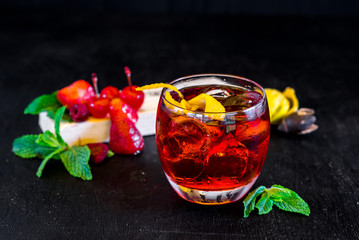 Red cocktail with ice and orange on black background