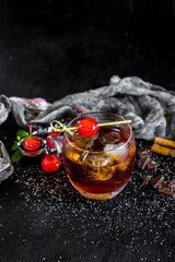 Glass of whiskey with ice and cherry on black background
