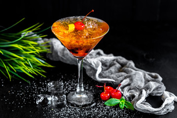 Sweet orange cocktail with cherry and ice on black background
