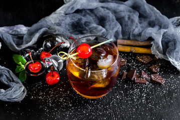 Glass of whiskey with ice and cherry on black background