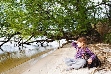 Little girl with backpack relaxing on the beach near by tree