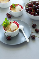 Cherry crumble with oatmeal and ice cream in bowl on grey wooden desk. Summer healthy food