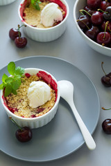 Cherry crumble with oatmeal and ice cream in bowl on grey wooden desk. Summer healthy food
