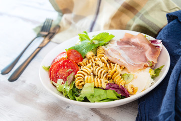 Salad with fusilli pasta accompanied tomatoes, mozzarella, smoked ham and italian cheese