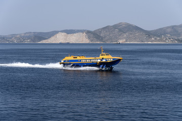 Yellow blue speedboat ferry at full speed on blue ocean water with skyline of mountain chain in the background - concept transport boat ship sea travel holiday