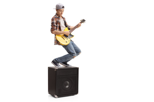Teenage boy standing on an amplifier and playing an electric guitar