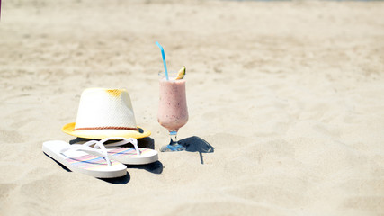 Strawberry fresh smoothie juice, hat and slippers near sea on sandy beach