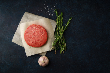 Raw minced beef patties on dark blue background with rosemary twigs and garlic. Top view, copy space