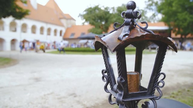 Retro street lamp made from hand shaped iron 4K. Dolly shot of lamp in focus without a light bulb inside, background castle park out of focus.