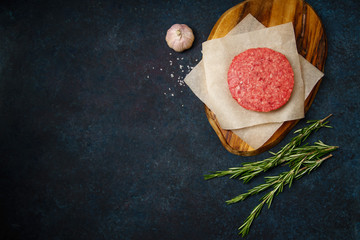 Raw minced beef patties on dark blue background with rosemary twigs and garlic. Top view, copy space