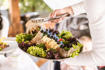 waitress in white uniform holding a plate of baked fish in a restaurant