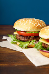 Classical burger with beef patty, tomatoes, cheese, onion, cucumber and lettuce served on wooden table against blue background