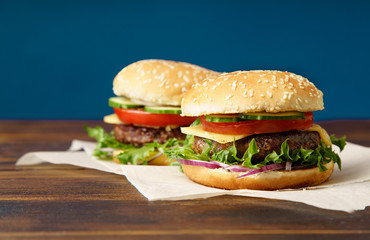 Classical burger with beef patty, tomatoes, cheese, onion, cucumber and lettuce served on wooden table against blue background