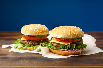 Classical burger with beef patty, tomatoes, cheese, onion, cucumber and lettuce served on wooden table against blue background