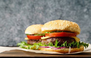 Classical burger with grilled meat, tomatoes, cheese, onion, cucumber and lettuce served on wooden table
