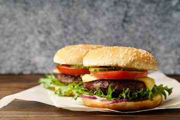 Classical burger with grilled meat, tomatoes, cheese, onion, cucumber and lettuce served on wooden table