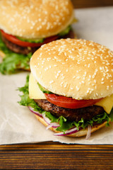 Classical burger with grilled meat, tomatoes, cheese, onion, cucumber and lettuce served on wooden table