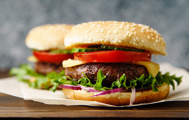 Classical burger with grilled meat, tomatoes, cheese, onion, cucumber and lettuce served on wooden table