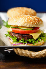 Classical burger with beef patty, tomatoes, cheese, onion, cucumber and lettuce served on wooden table against blue background