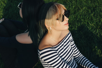 stylish young women sitting on green grass back to back