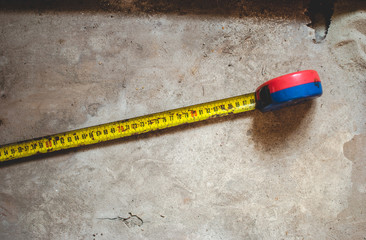 Closeup of an old rusty yellow measuring tape with black numbers measuring centimeters. Item laying on the dusty floor of the storage