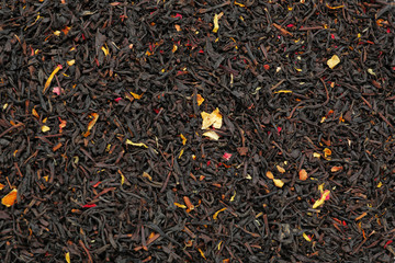 Dry black tea leaves with fruits and petals as background