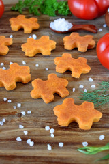 Puzzle shaped salty cookies with paprika and tomato paste on a wooden board surrounded by the ingredients