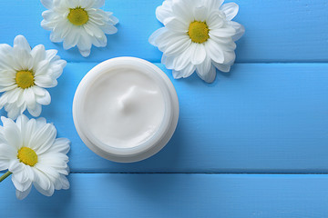 Fototapeta na wymiar Jar of body cream and beautiful flowers on color background