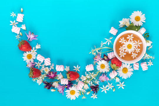 Cup of tea with fresh strawberries, marshmallows and flowers blossom bouquets on blue surface