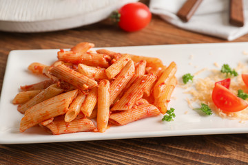 Plate of tasty penne pasta with tomato sauce on wooden table, closeup