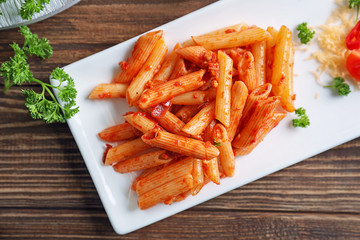 Plate of tasty penne pasta with tomato sauce on wooden table, top view