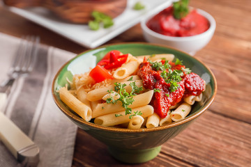 Bowl with tasty penne pasta and bolognese sauce on wooden table