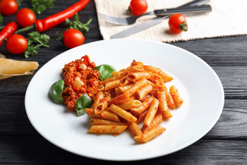 Plate with tasty penne pasta and bolognese sauce on wooden table