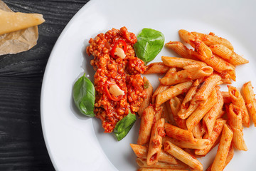 Tasty penne pasta with bolognese sauce on plate, closeup