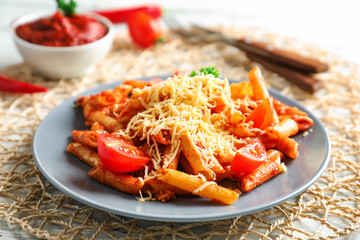 Plate of tasty penne pasta with tomato sauce on table
