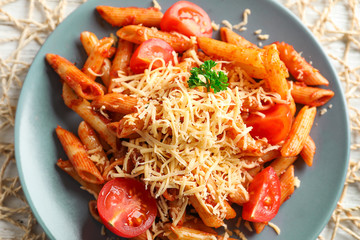 Tasty penne pasta with tomato sauce and grated cheese on plate, closeup