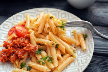 Tasty penne pasta with bolognese sauce on plate, closeup