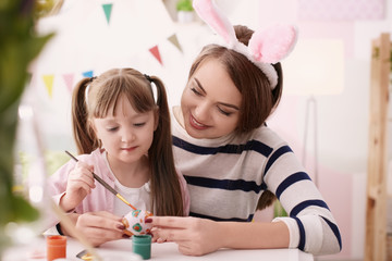 Mother painting Easter eggs with her daughter at table