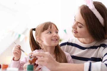 Mother painting Easter eggs with her daughter at table